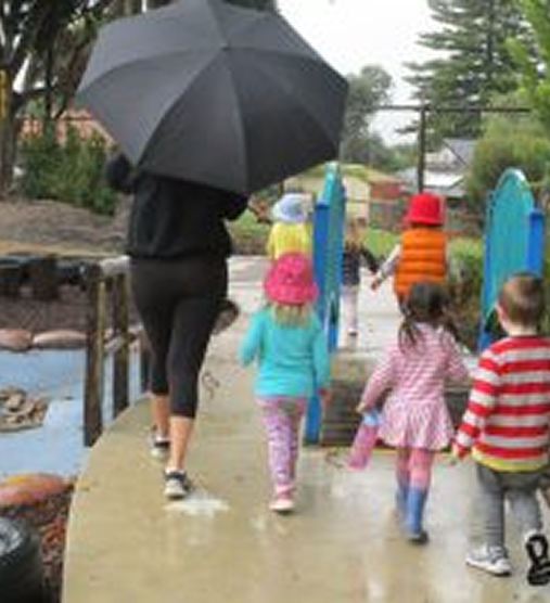 A woman holds an umbrella while guiding children along a wet path, showcasing a rainy day outing.