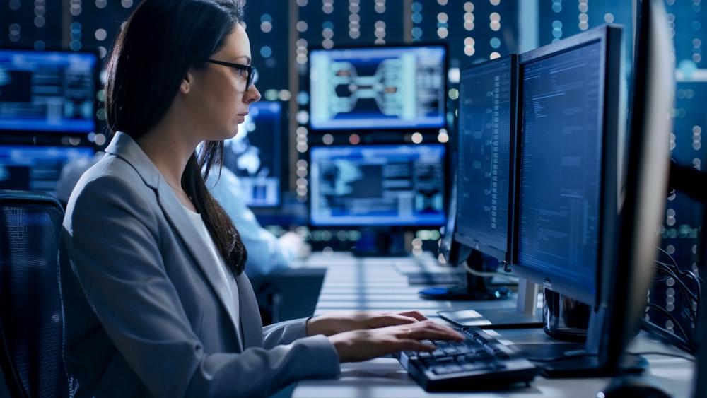 Woman working on multiple monitors in a modern office providing cyber security Perth services for government industries.